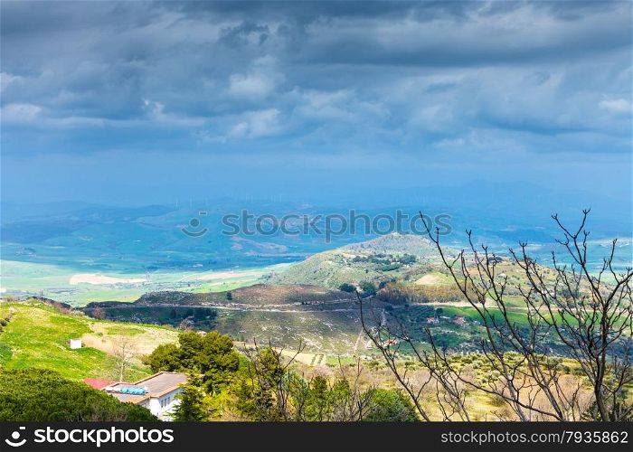 dark blue rainy clouds over green sicilian hills in spring, Aidone, Italy