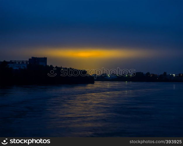 Dark blue sky with yellow city lights. View from the river. Night sky with reflection of the yellow lights of the city