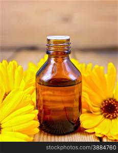 Dark bottle of aromatic oil, yellow marigold flowers on a background of wooden planks