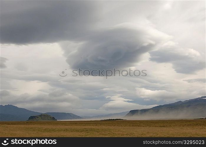 Dark clouded skies and farmland with mountain landscape