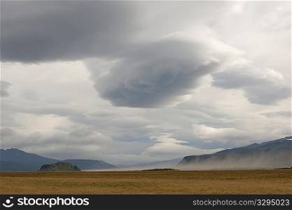 Dark clouded skies and farmland with mountain landscape