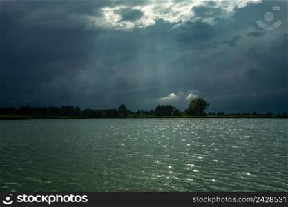 Dark clouds and sunbeams above the lake water, summer evening