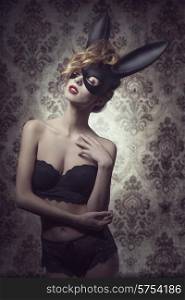 Dark easter portrait of sensual curly woman with romantic expression posing with mysterious bunny mask and lace lingerie