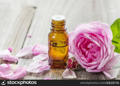 Dark glass vial with rose essential oil and flower of pink rose on a wooden background, with space for text