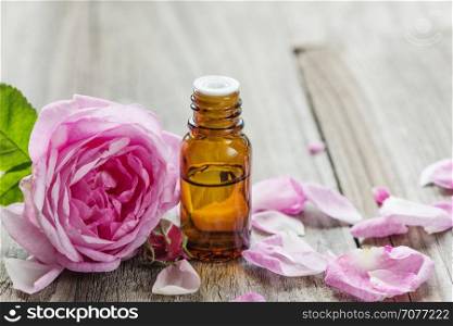 Dark glass vial with rose essential oil and flower of pink rose on a wooden background