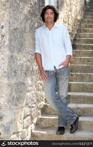 Dark haired man leaning against stone wall