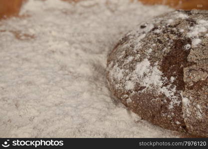 Dark homemade bread lies on flour on a wooden tray.. Dark homemade bread lies on flour on a wooden tray. Composition on a beautiful tablecloths canvas. Photos for magazines about cooking.