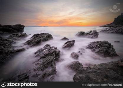 Dark of soft waves of ocean in sunset with stones on the beach foreground at Khao Laem Ya Mu Ko Samet National Park Rayong, Thailand. Seascape long exposure shot
