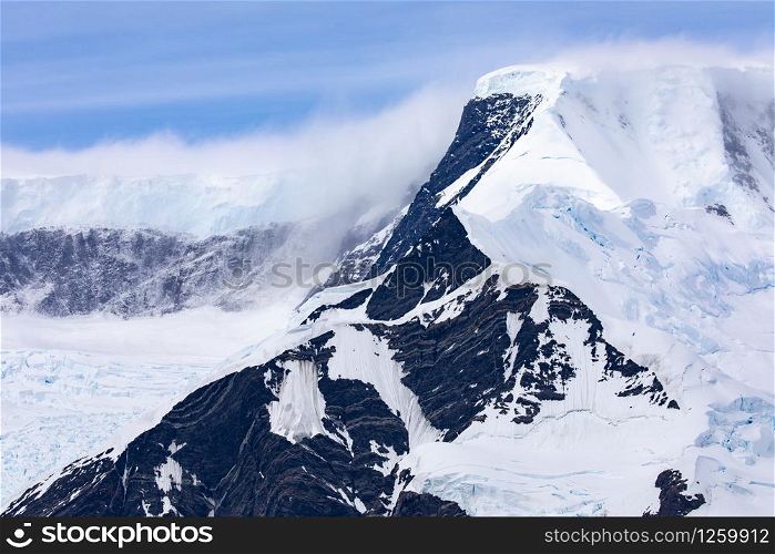 Dark peak of high mountain covered with snow and glacier tongue in glacier bed in Antarctica