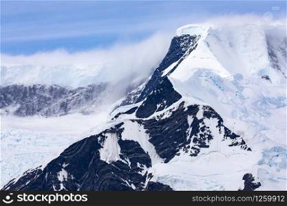 Dark peak of high mountain covered with snow and glacier tongue in glacier bed in Antarctica