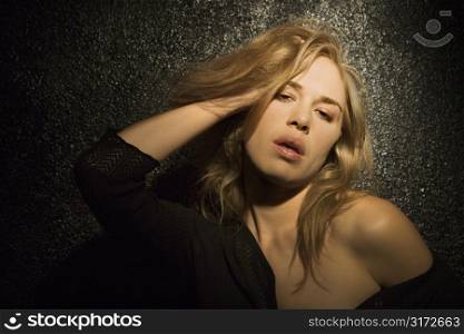 Dark portrait of sexy Caucasian mid-adult woman with hand in hair making sultry expression.