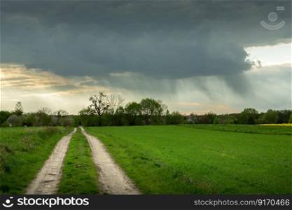 Dark rain cloud over the green field by the road, cloudy spring day