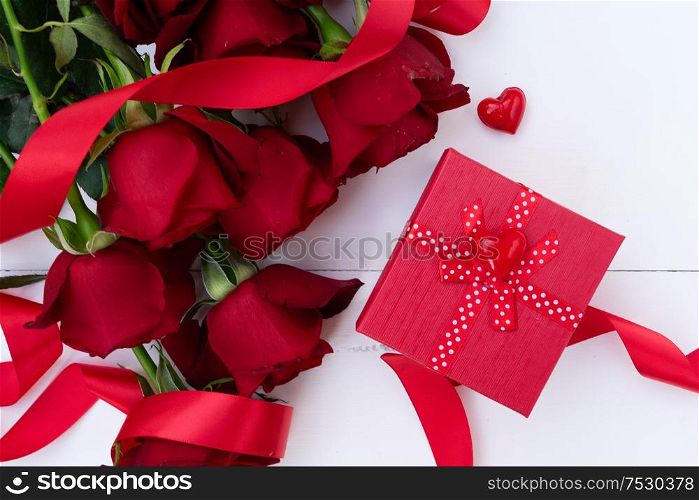 Dark Red buds of valentines day festive roses with gift box on white wood. Red blooming roses on wood