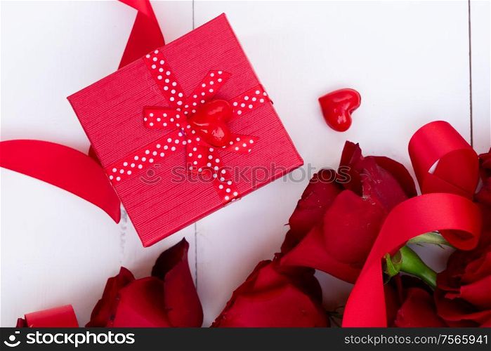 Dark Red buds of valentines day festive roses with gift box on white wood. Red blooming roses on wood