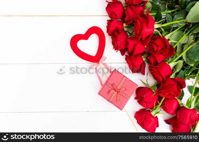 Dark Red buds of valentines day festive roses with heart and gift box on white wood with copy space. Red blooming roses on wood