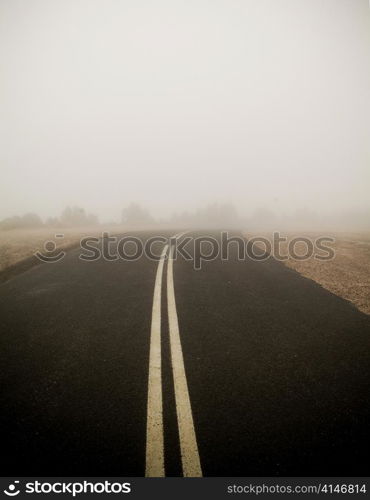 Dark road with double lines disappears into very thick fog