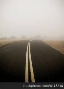 Dark road with double lines disappears into very thick fog