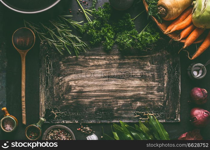 Dark rustic food background frame with vegetarian ingredients: root vegetables, red onion, spices, cooking spoon and seasoning, top view. Clean food. Paleo diet. Healthy eating concept. Copy space