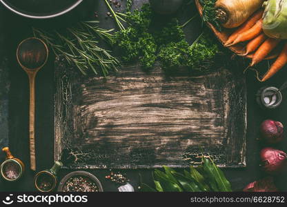 Dark rustic food background frame with vegetarian ingredients: root vegetables, red onion, spices, cooking spoon and seasoning, top view. Clean food. Paleo diet. Healthy eating concept. Copy space