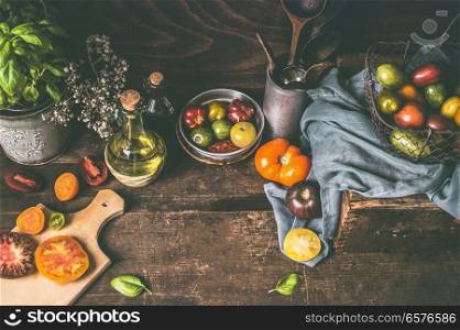 Dark rustic wooden kitchen table with colorful farm tomatoes, ingredients and cooking tools. Country style food background, still life, top view. Place for your design, recipes , text or products