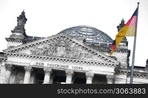 Das deutsche Parlament in Berlin, der Reichstag, ist farblich isoliert. Der Wind weht leicht, die Fahne als einziges farbiges Element bewegt sich. Menschen laufen durch die Kuppel auf dem Dach.