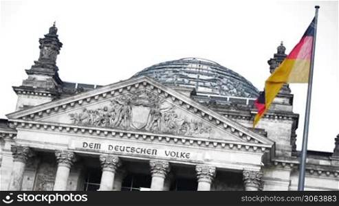 Das deutsche Parlament in Berlin, der Reichstag, ist farblich isoliert. Der Wind weht leicht, die Fahne als einziges farbiges Element bewegt sich. Menschen laufen durch die Kuppel auf dem Dach.