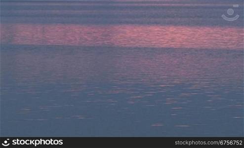 Das Wasser eines See&acute;s schimmert blau-rosa im Abendlicht