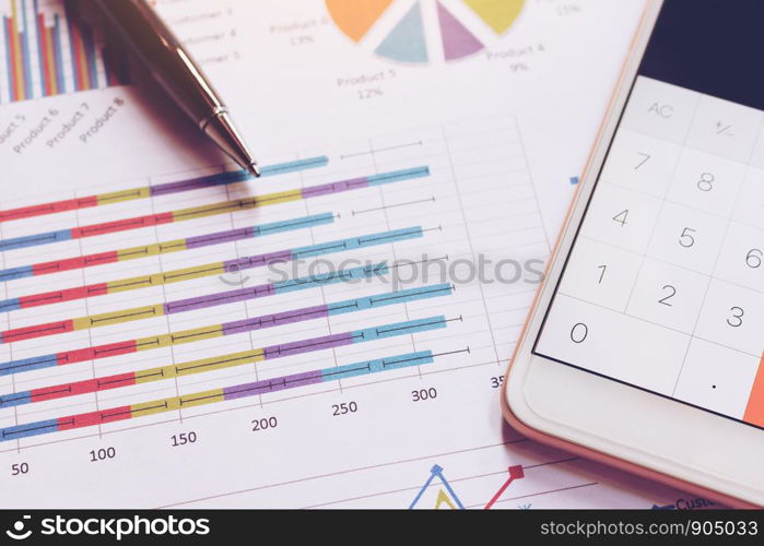 Data analyzing with calculator in smart phone and pen on charts and graph.