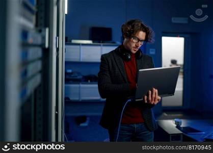 Data engineer holding laptop while working with supercomputer in server room. Technician doing motherboard or firewall system assessment work. Data engineer holding laptop while working with supercomputer in server room