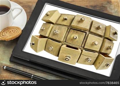 data storage or cloud computing concept - vintage apothecary drawer cabinet in fish eye lens perspective on a digital tablet with cup of coffee