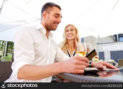date, people, payment and finances concept - happy couple with credit card and wine glasses paying bill at restaurant