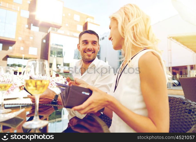 date, people, payment and finances concept - happy couple with wallet and wine glasses paying bill at restaurant