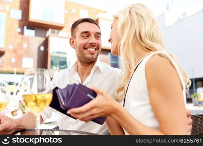 date, people, payment and finances concept - happy couple with wallet and wine glasses paying bill at restaurant