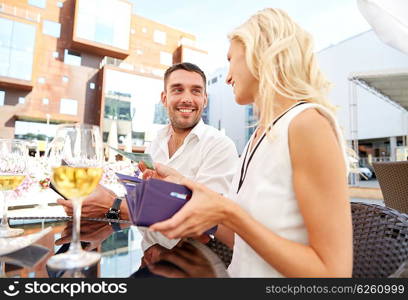 date, people, payment and finances concept - happy couple with wallet and wine glasses paying bill at restaurant