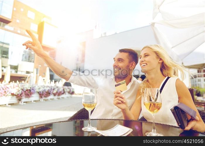 date, people, payment and finances concept - happy couple with wallet, credit card and wine glasses calling waiter for bill payment at restaurant