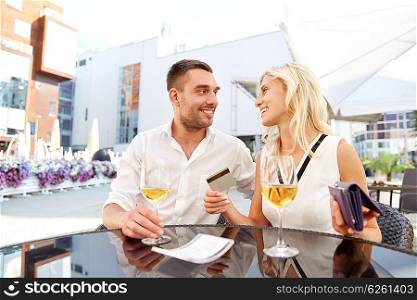 date, people, payment and finances concept - happy couple with wallet, credit card and wine glasses paying bill at restaurant