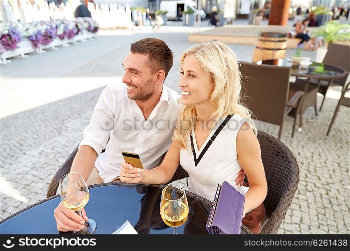 date, people, payment and finances concept - happy couple with wallet, credit card and wine glasses paying bill at restaurant