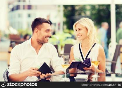 date, people, payment and financial independence concept - happy couple with cash money in wallets and wine glasses paying bill at restaurant