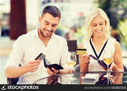 date, people, payment and financial independence concept - happy couple with credit cards in wallets and wine glasses paying bill at restaurant