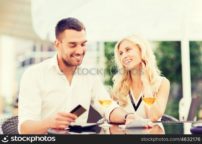 date, people, payment and relations concept - happy couple with credit card, bill and wine glasses at restaurant terrace