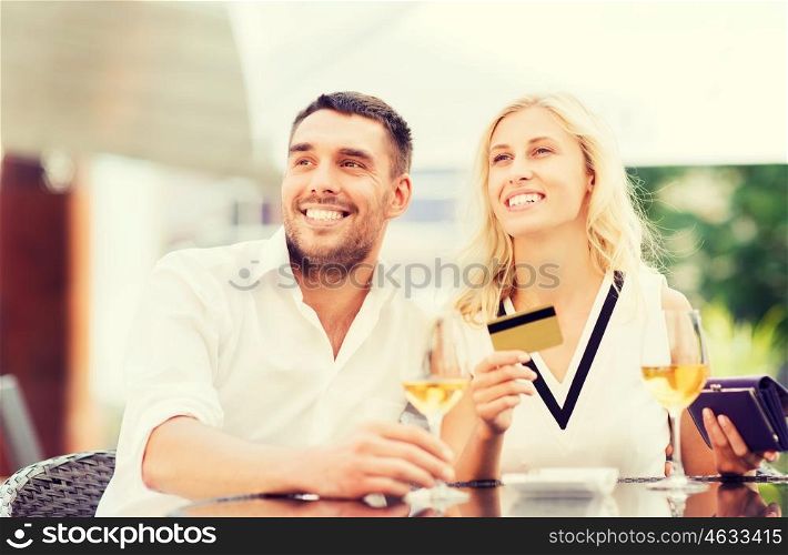 date, people, payment and relations concept - happy couple with credit card, bill and wine glasses at restaurant terrace