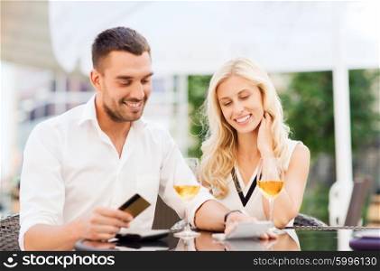 date, people, payment and relations concept - happy couple with credit card, bill and wine glasses at restaurant terrace