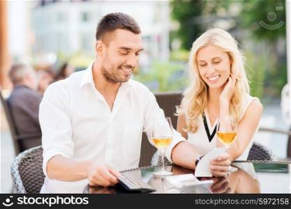date, people, payment, holidays and relations concept - happy couple with wallet and wine glasses looking at bill at restaurant terrace