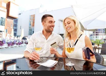 date, people, relations and finances concept - happy couple with wallet, credit card and wine glasses paying bill at restaurant
