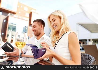 date, people, relations, payment and finances concept - happy couple with wallet and wine glasses paying bill at restaurant