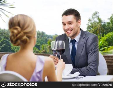 dating, celebration and valentines day concept - smiling young couple clinking glasses of non-alcoholic red wine and looking at each other at restaurant over summer background. young couple with glasses of wine at restaurant