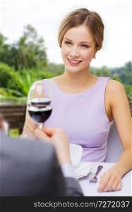 dating, celebration and valentines day concept - smiling young woman clinking glass of non-alcoholic red wine with her man at restaurant over summer background. woman drinking wine with her man at restaurant