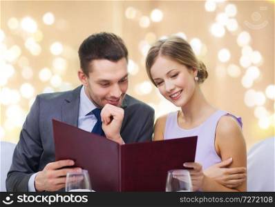 dating, luxury and people concept - happy couple with menu at restaurant over festive lights on beige background. couple with menu at restaurant