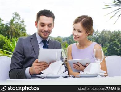 dating, luxury and people concept - happy couple with menus on tablet pc computers at restaurant over summer background. couple with menu on tablet computers at restaurant