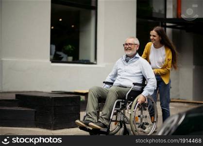 Daughter and disabled father in wheelchair go for a walk. Paralyzed people and disability, handicap overcoming. Handicapped male person and young female guardian in public place. Daughter and disabled father go for a walk